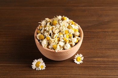 Dry and fresh chamomile flowers in bowl on wooden table