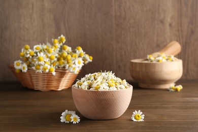 Photo of Dry and fresh chamomile flowers in bowl on wooden table