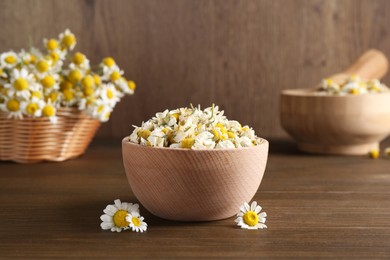 Photo of Dry and fresh chamomile flowers in bowl on wooden table