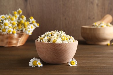 Dry and fresh chamomile flowers in bowl on wooden table