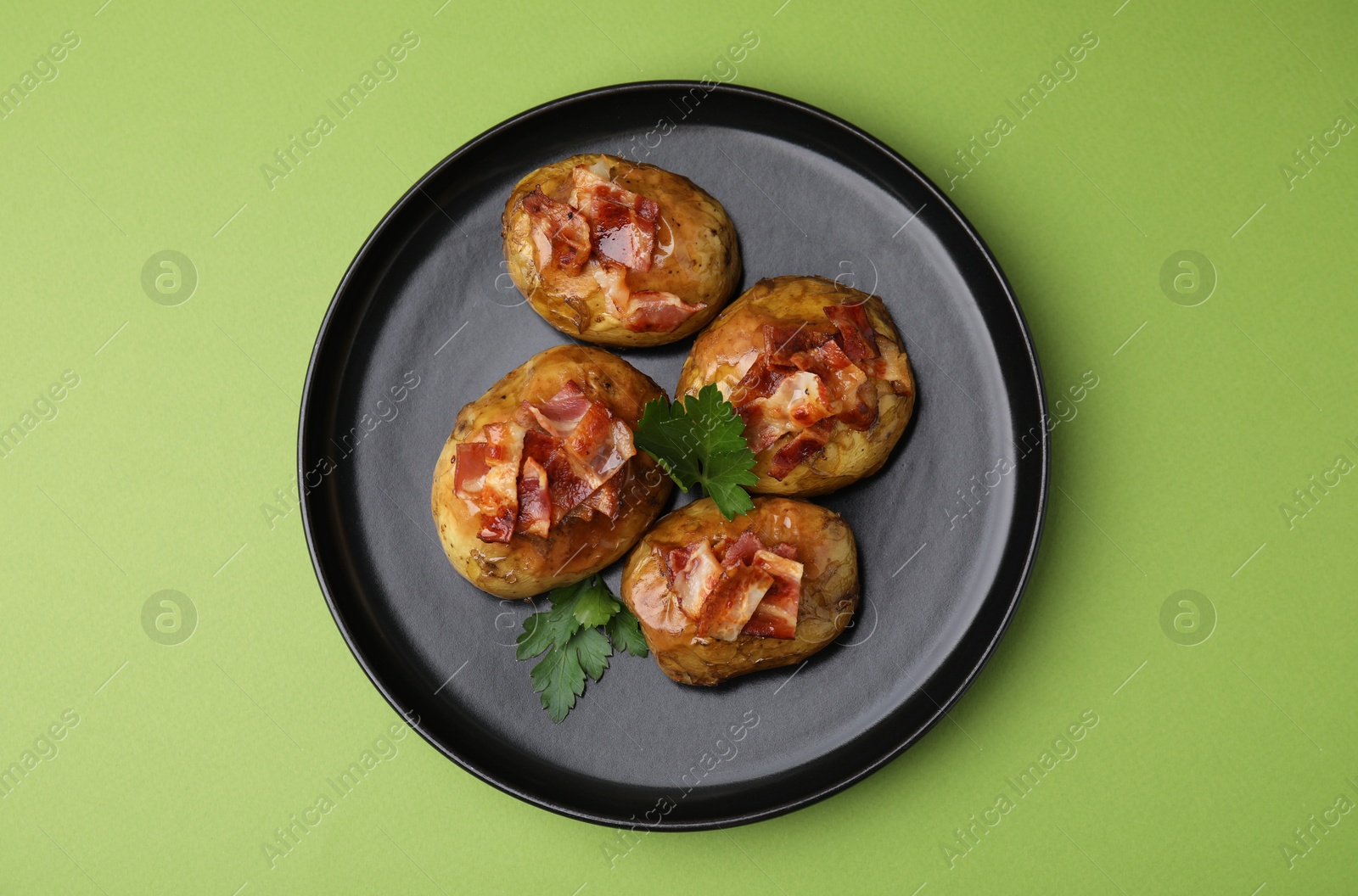 Photo of Delicious baked potatoes with bacon and parsley on green background, top view