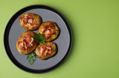 Delicious baked potatoes with bacon and parsley on green background, top view. Space for text