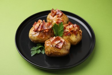 Photo of Delicious baked potatoes with bacon and parsley on green background, closeup