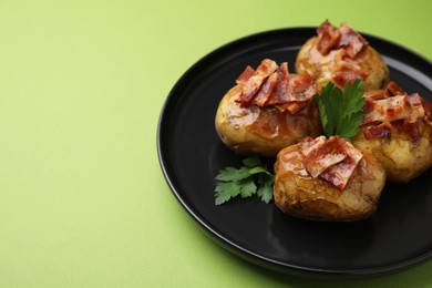 Photo of Delicious baked potatoes with bacon and parsley on green background, closeup. Space for text