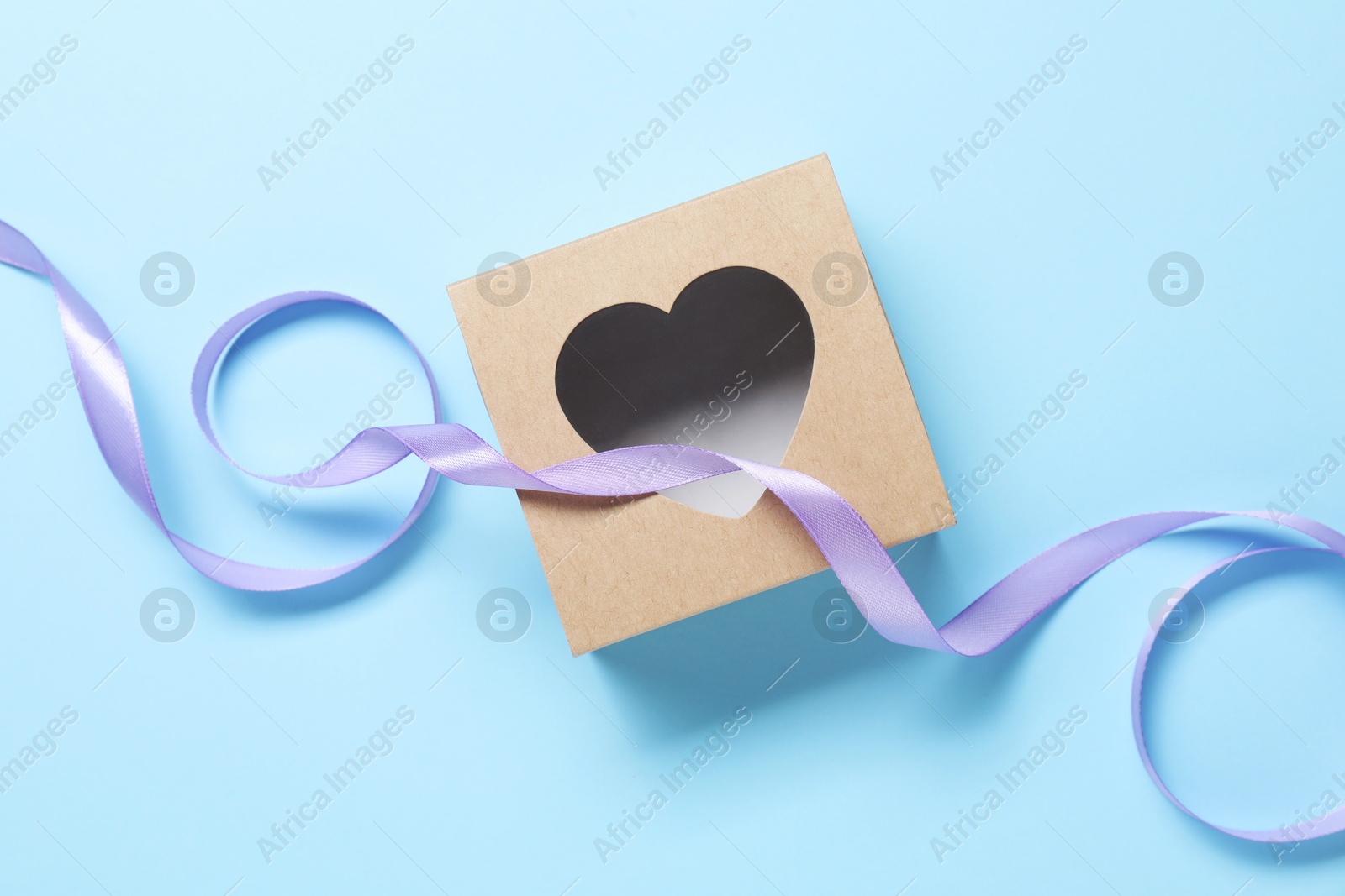 Photo of Beautiful violet ribbon and gift box with heart on light blue background, flat lay