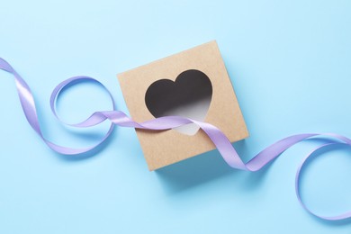 Photo of Beautiful violet ribbon and gift box with heart on light blue background, flat lay