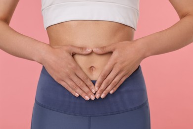 Healthy digestion. Woman making heart shape with hands near her belly on pink background, closeup