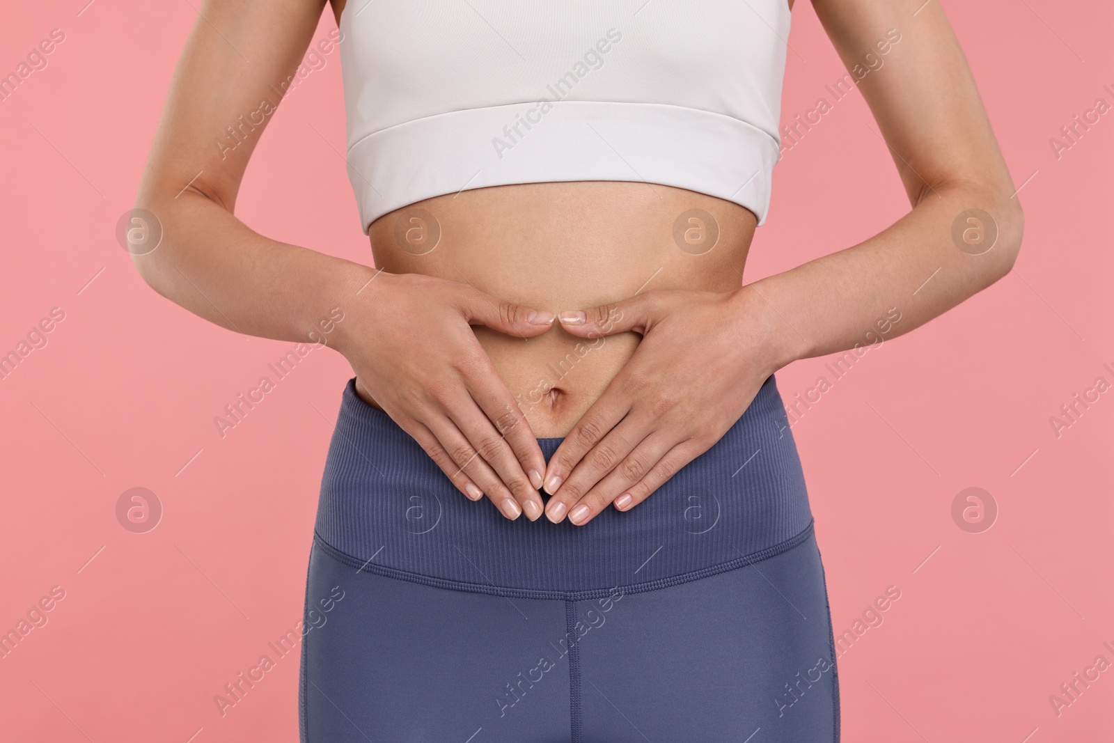 Photo of Healthy digestion. Woman making heart shape with hands near her belly on pink background, closeup