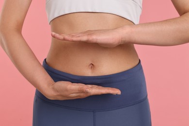 Photo of Healthy digestion. Woman holding something near her belly on pink background, closeup