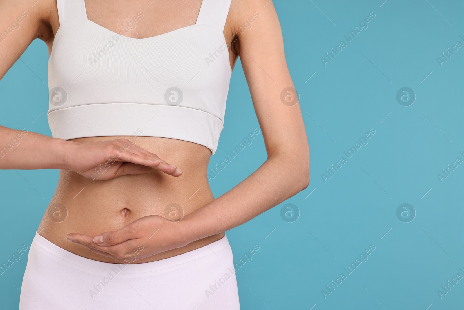 Photo of Healthy digestion. Woman holding something near her belly on light blue background, closeup. Space for text