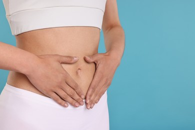 Photo of Healthy digestion. Woman making heart shape with hands near her belly on light blue background, closeup. Space for text