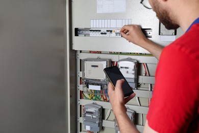 Technician worker with smartphone inspecting electricity meter, closeup