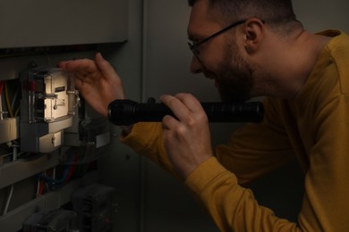 Man with flashlight checking electricity meter indoors