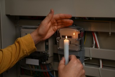 Photo of Man with candle checking electricity meter indoors, closeup