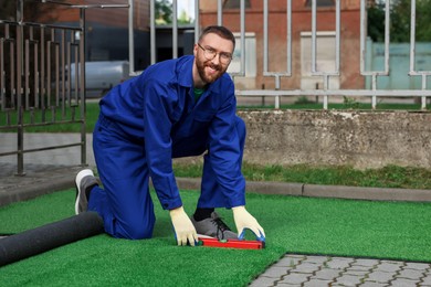 Happy young man in uniform installing artificial turf outdoors