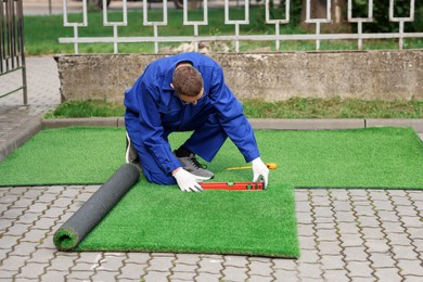 Photo of Young man in uniform installing artificial turf outdoors