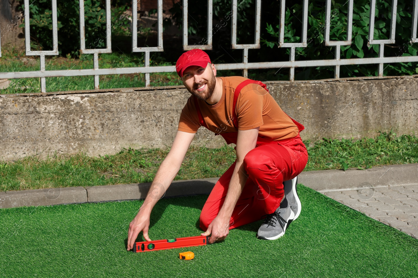 Photo of Happy young man installing artificial turf outdoors