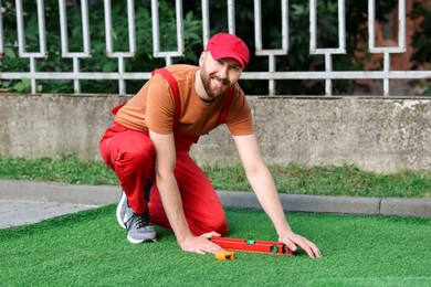 Photo of Happy young man installing artificial turf outdoors