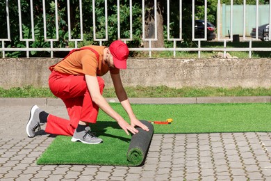 Young man in uniform installing artificial turf outdoors