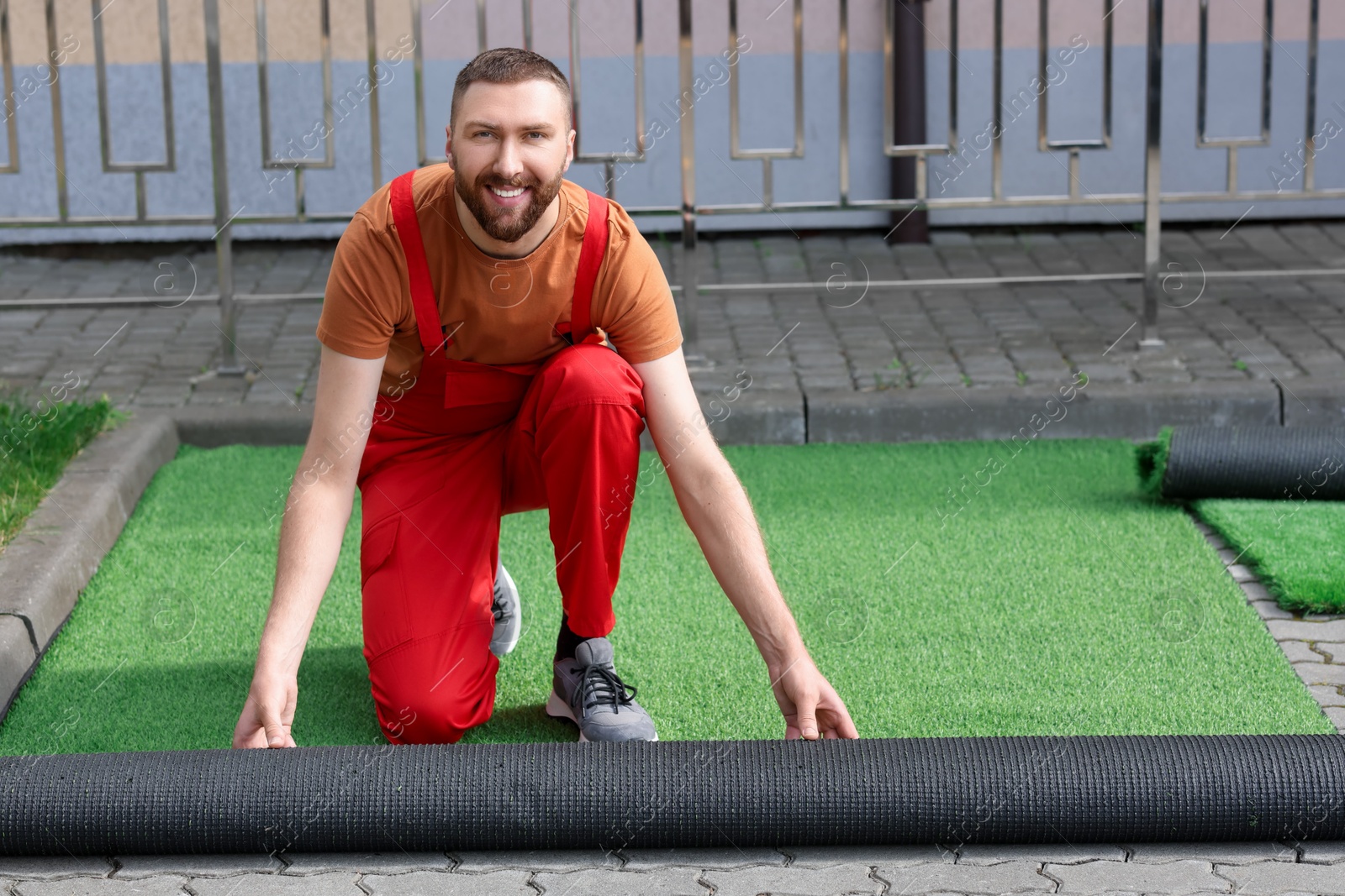 Photo of Happy young man in uniform installing artificial turf outdoors