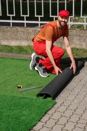 Photo of Happy young man in uniform installing artificial turf outdoors