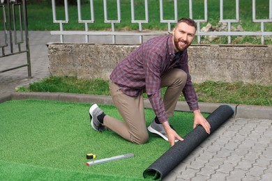 Photo of Happy young man installing artificial turf outdoors