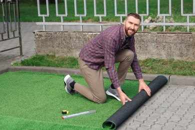 Happy young man installing artificial turf outdoors