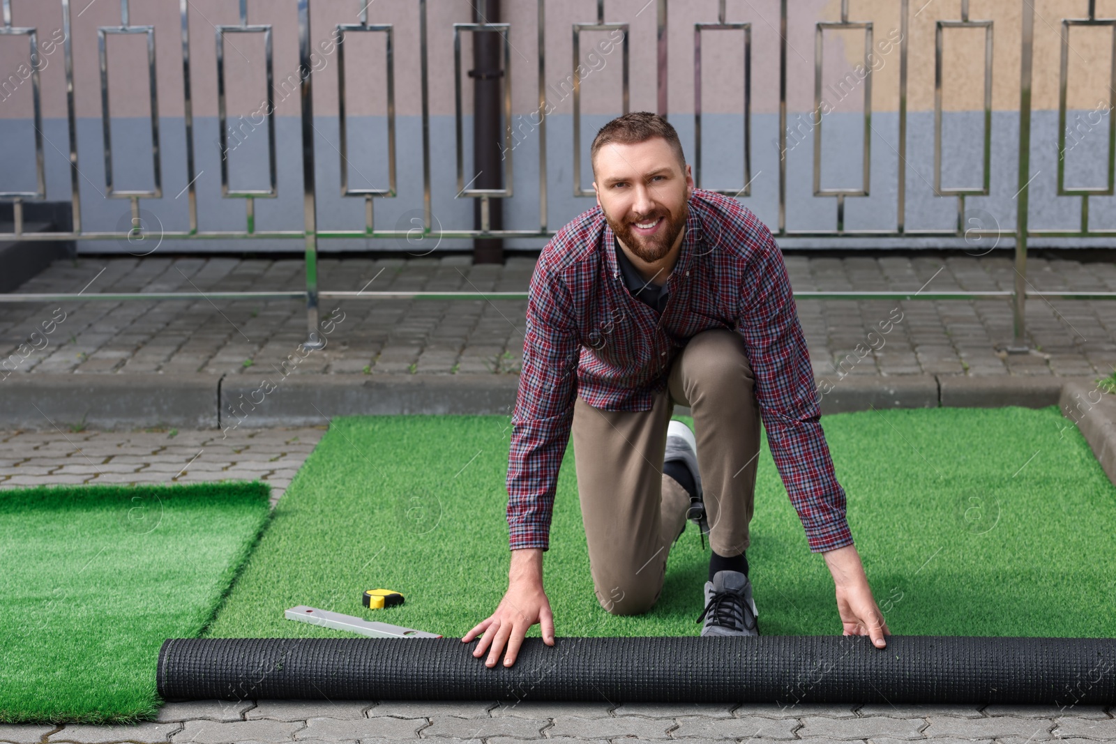 Photo of Happy young man installing artificial turf outdoors