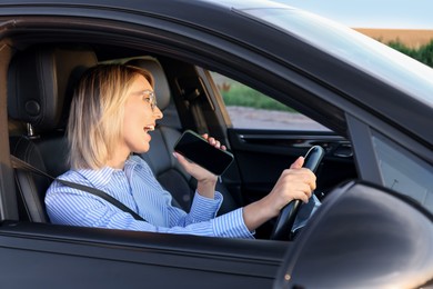 Woman with smartphone singing in car, view from outside