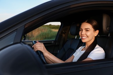 Photo of Smiling young woman holding steering wheel while driving car, view from outside