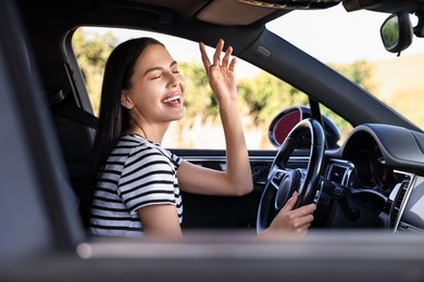 Smiling young woman having fun while driving car, view from outside