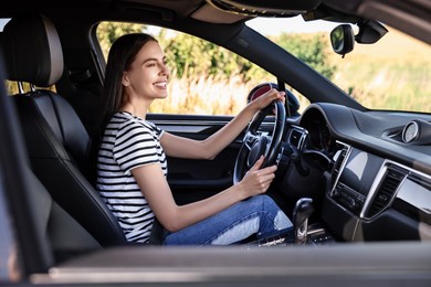 Smiling young woman holding steering wheel while driving car, view from outside