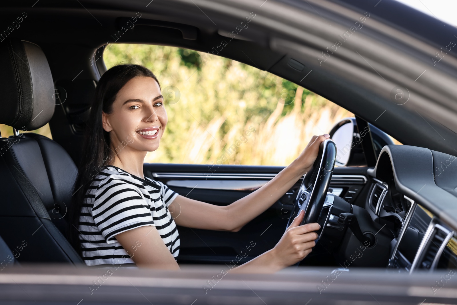 Photo of Smiling young woman holding steering wheel while driving car, view from outside