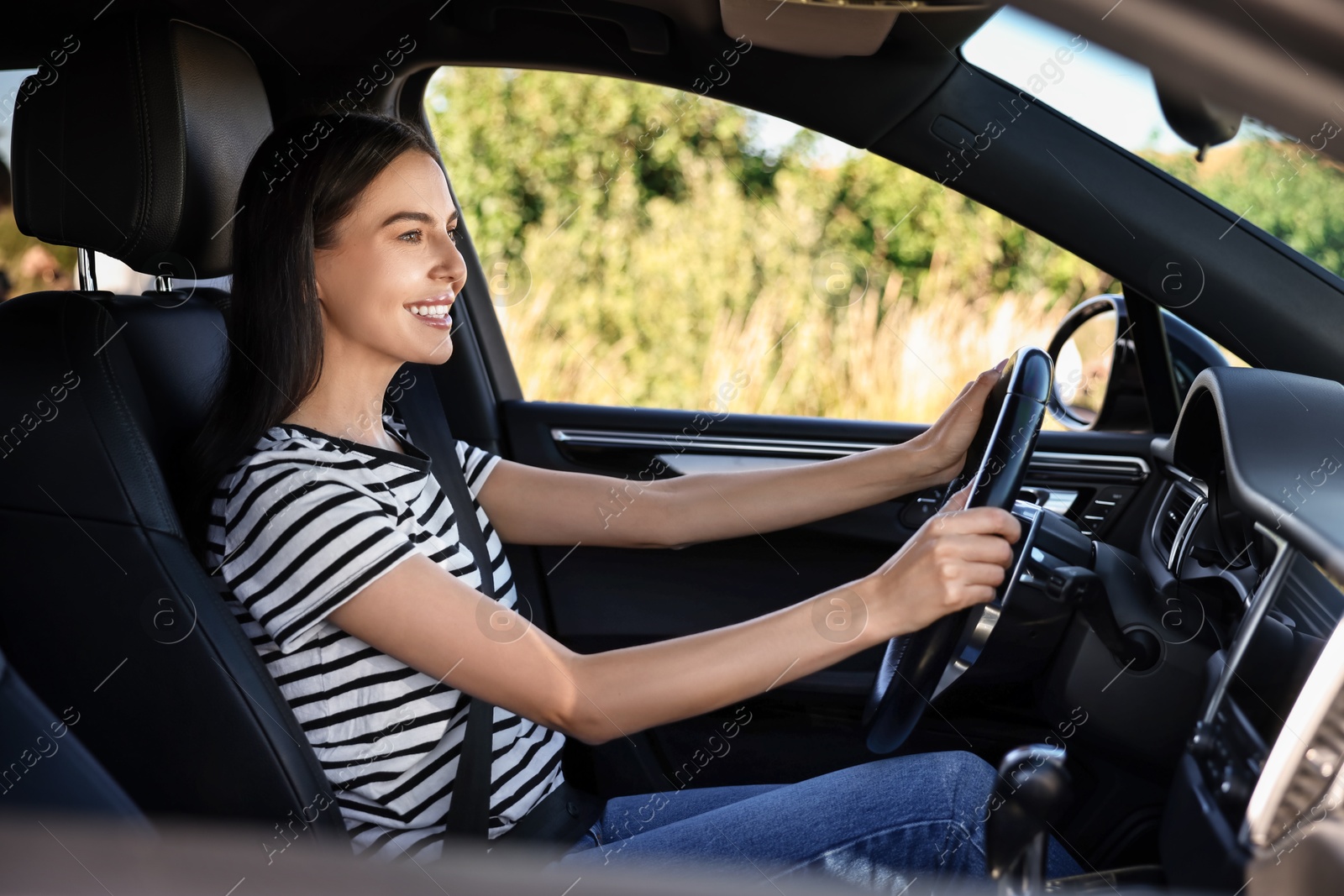 Photo of Smiling young woman holding steering wheel while driving car, view from outside