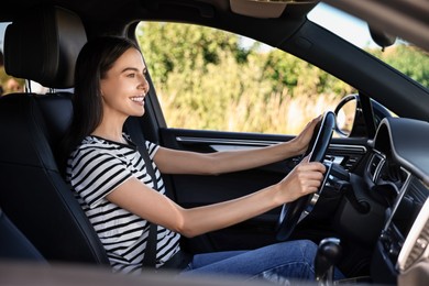 Smiling young woman holding steering wheel while driving car, view from outside