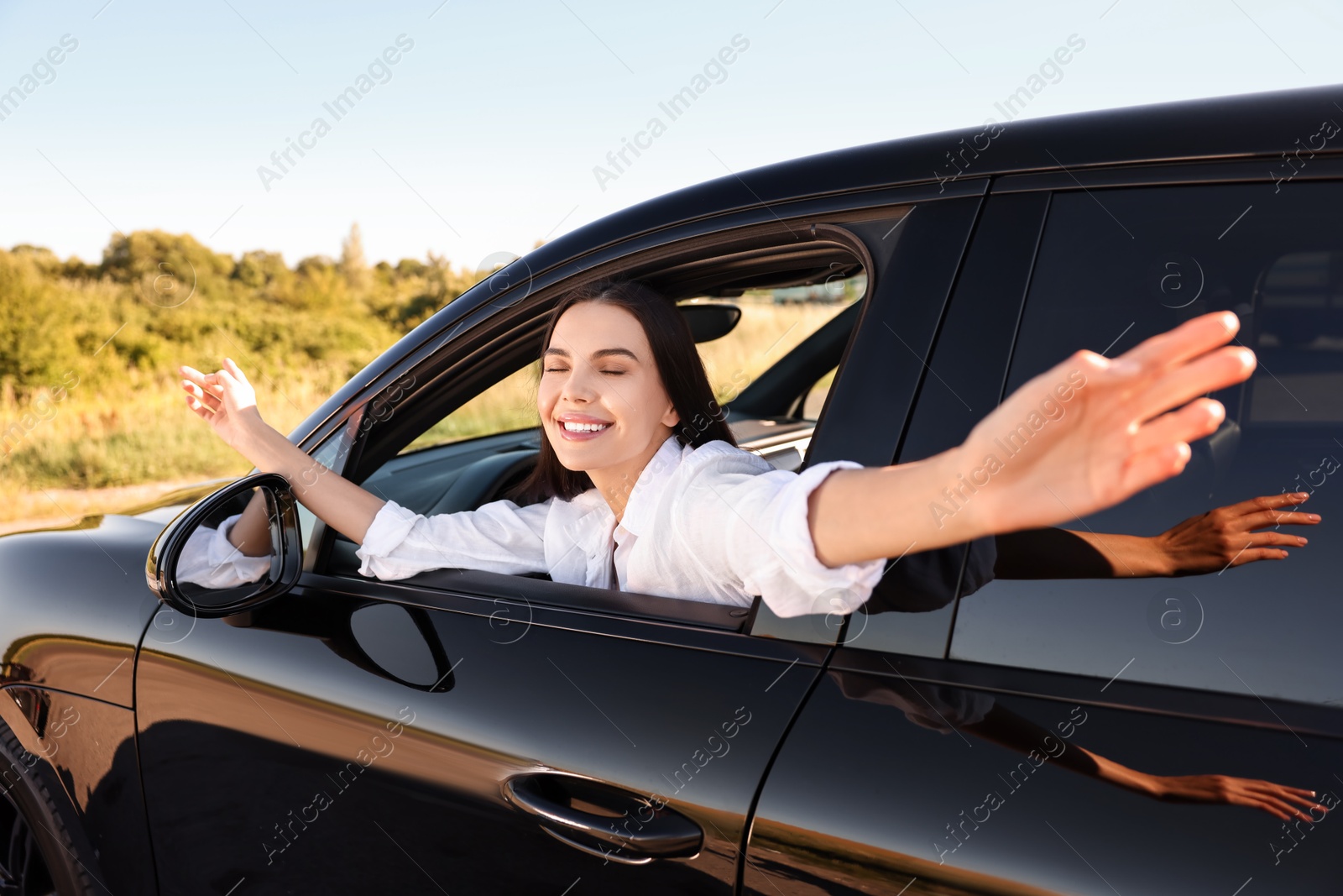 Photo of Smiling young woman leaning out of car window, view from outside. Enjoying trip