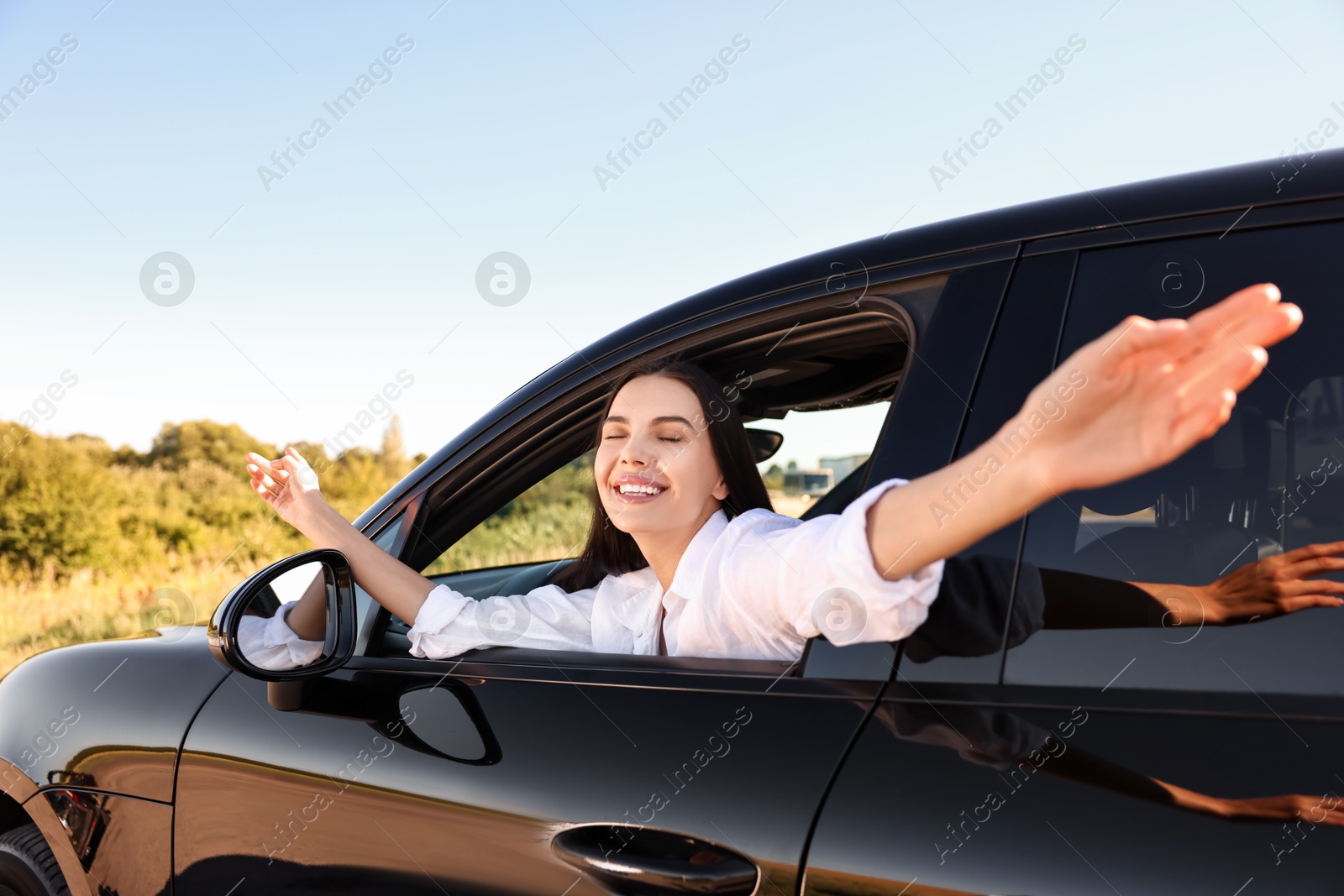 Photo of Smiling young woman leaning out of car window, view from outside. Enjoying trip