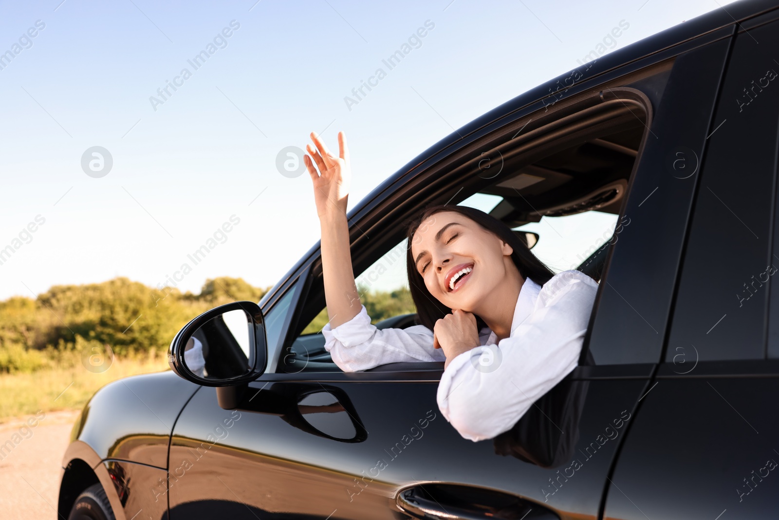 Photo of Smiling young woman leaning out of car window, view from outside. Enjoying trip