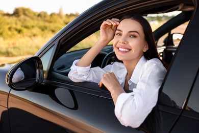 Smiling young woman leaning out of car window, view from outside. Enjoying trip