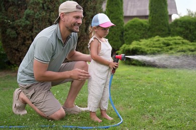 Photo of Father and his daughter watering lawn with hose in backyard