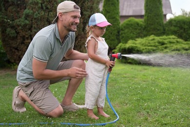 Father and his daughter watering lawn with hose in backyard