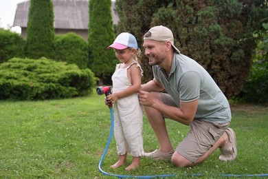 Photo of Father and his daughter watering lawn with hose in backyard, space for text