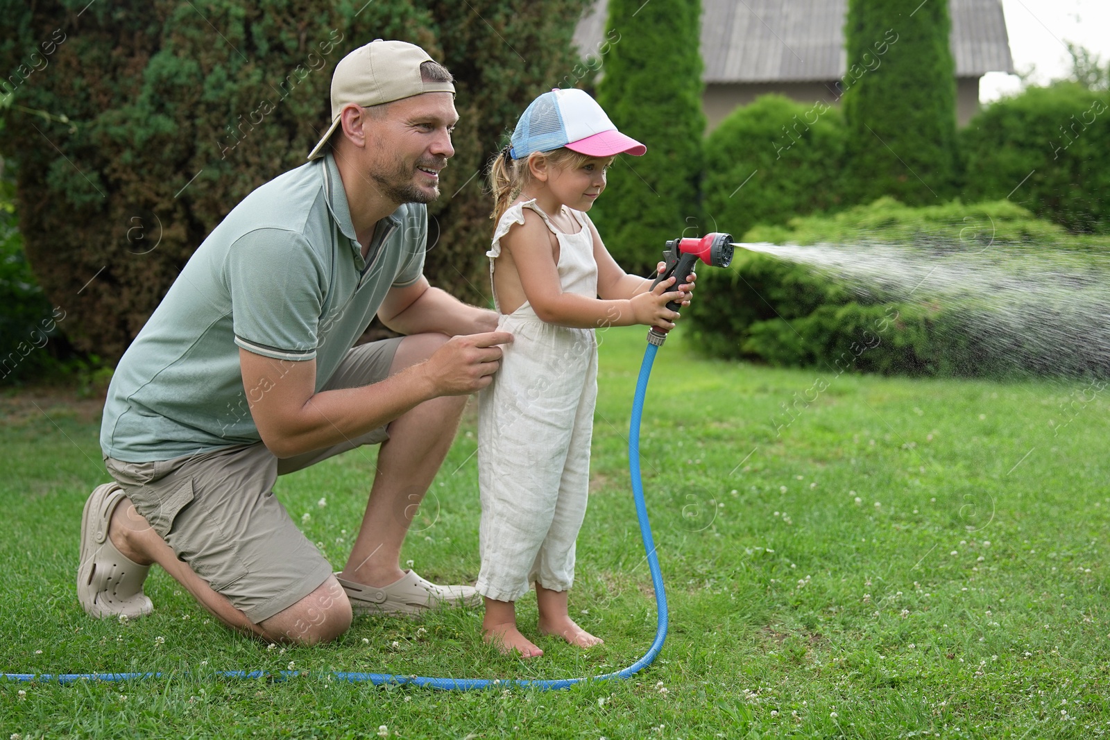 Photo of Father and his daughter watering lawn with hose in backyard