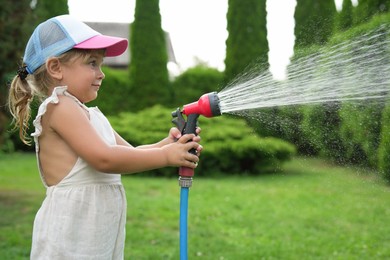 Photo of Little girl watering lawn with hose in backyard