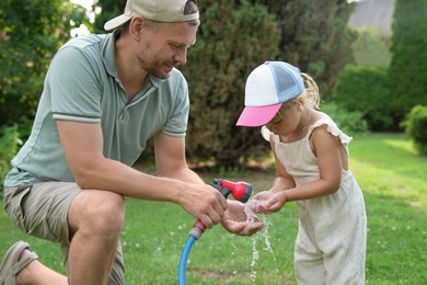 Photo of Father holding hose while his daughter drinking water in backyard