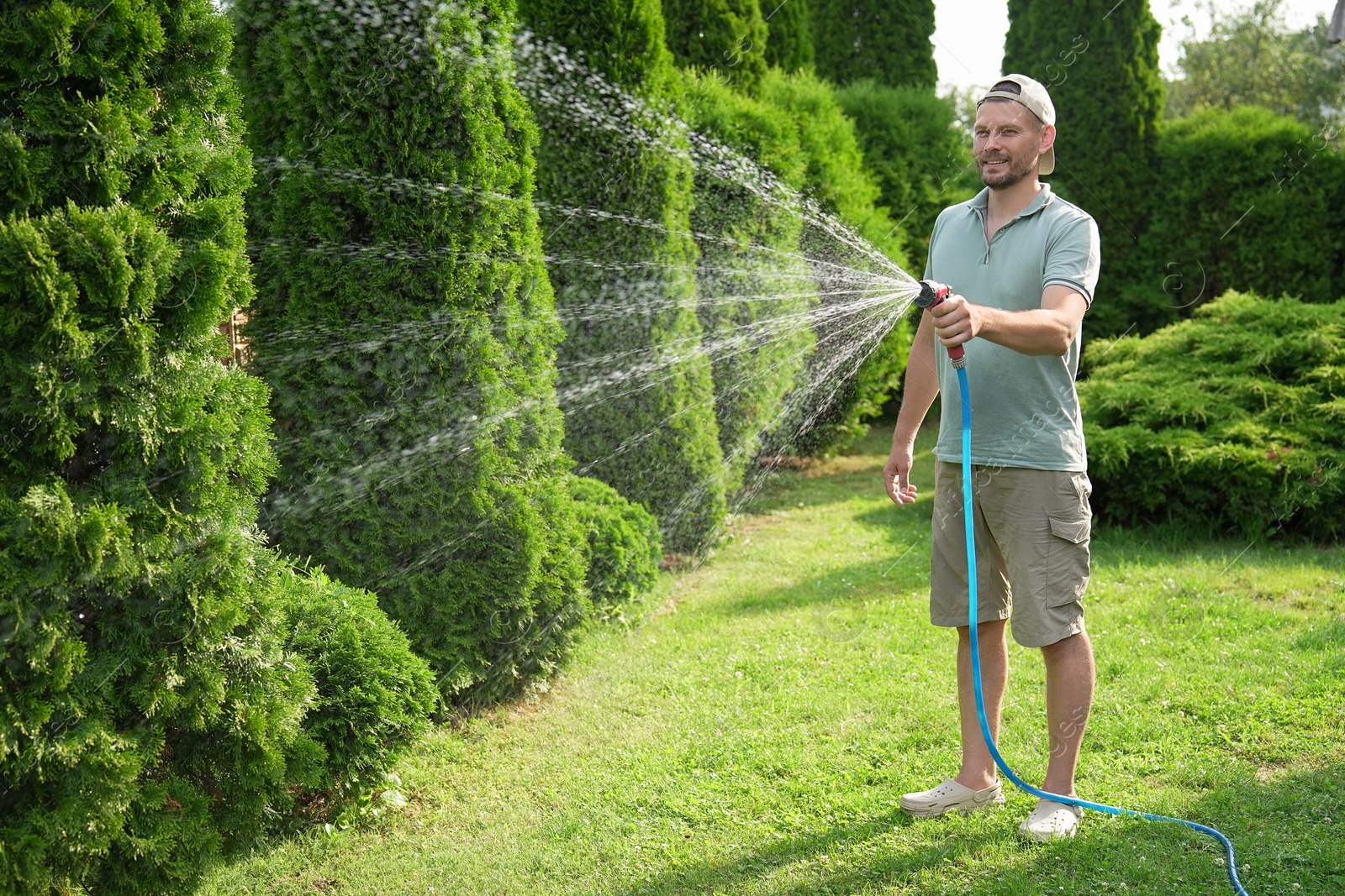 Photo of Man watering lawn with hose in backyard