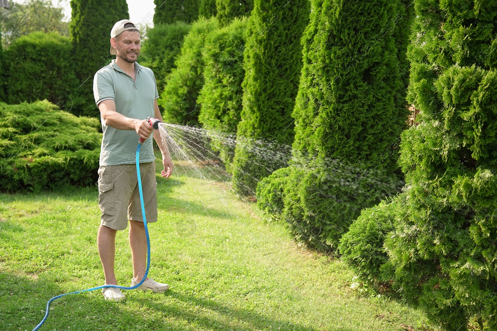 Photo of Man watering lawn with hose in backyard