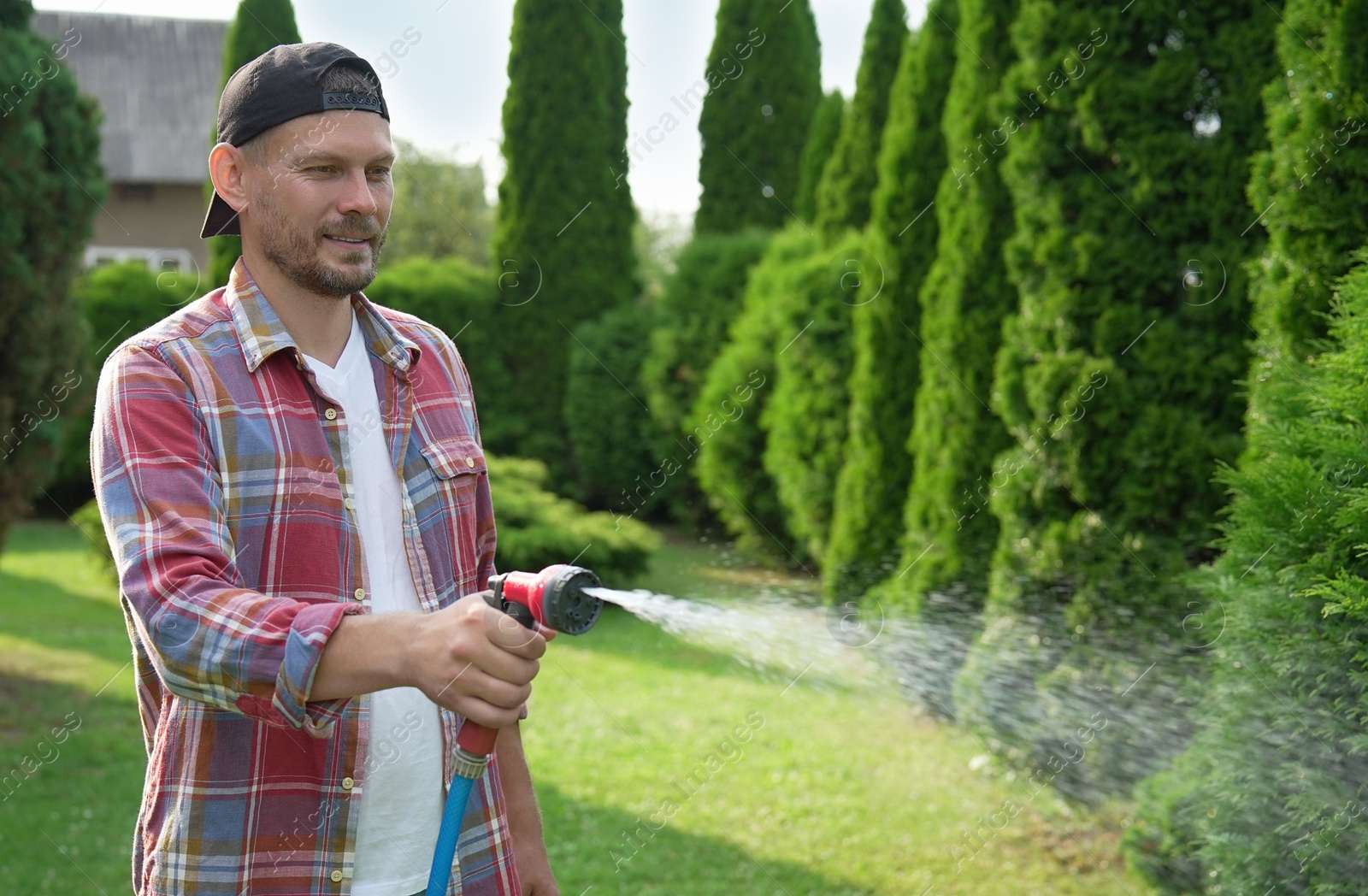 Photo of Man watering lawn with hose in backyard