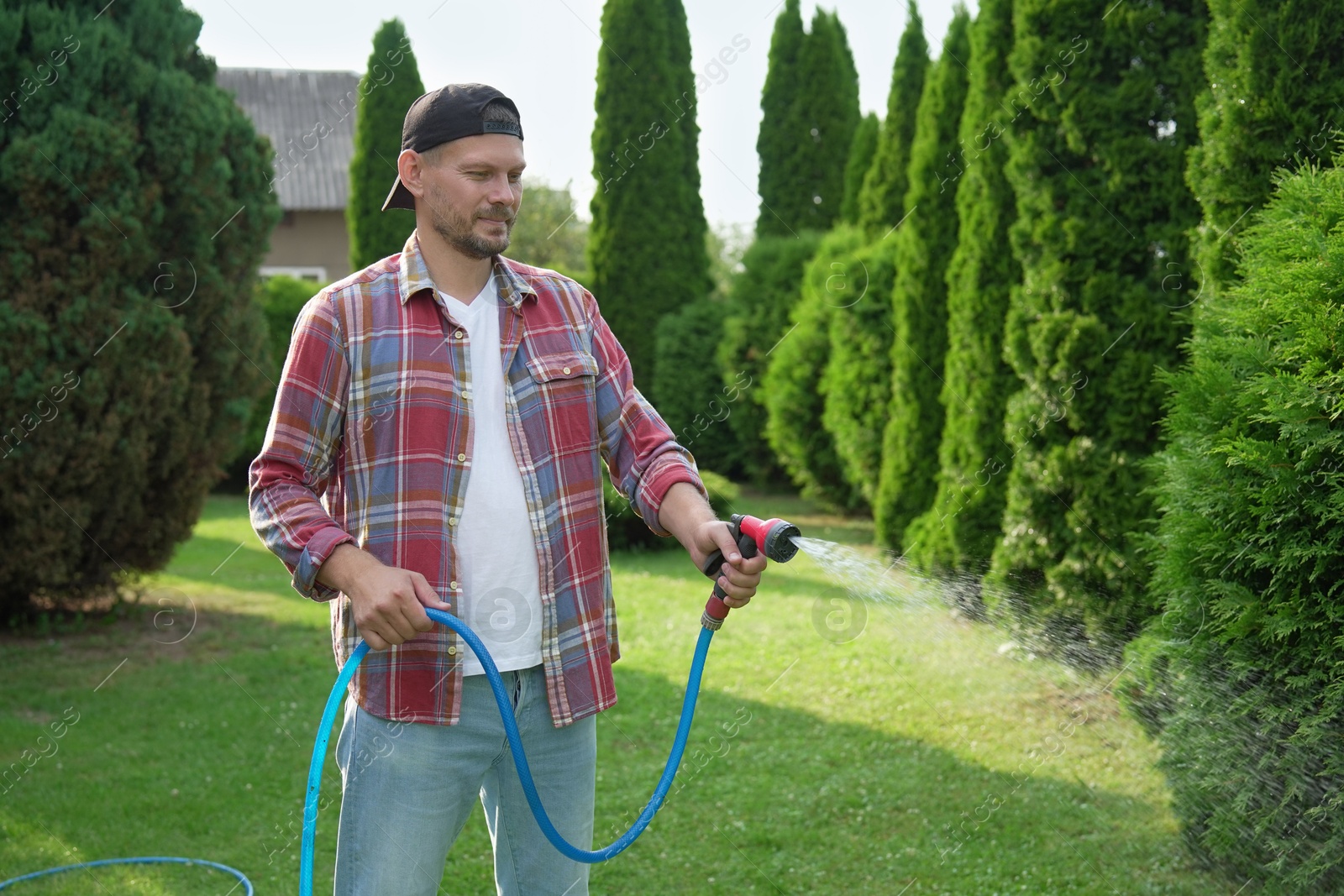 Photo of Man watering lawn with hose in backyard