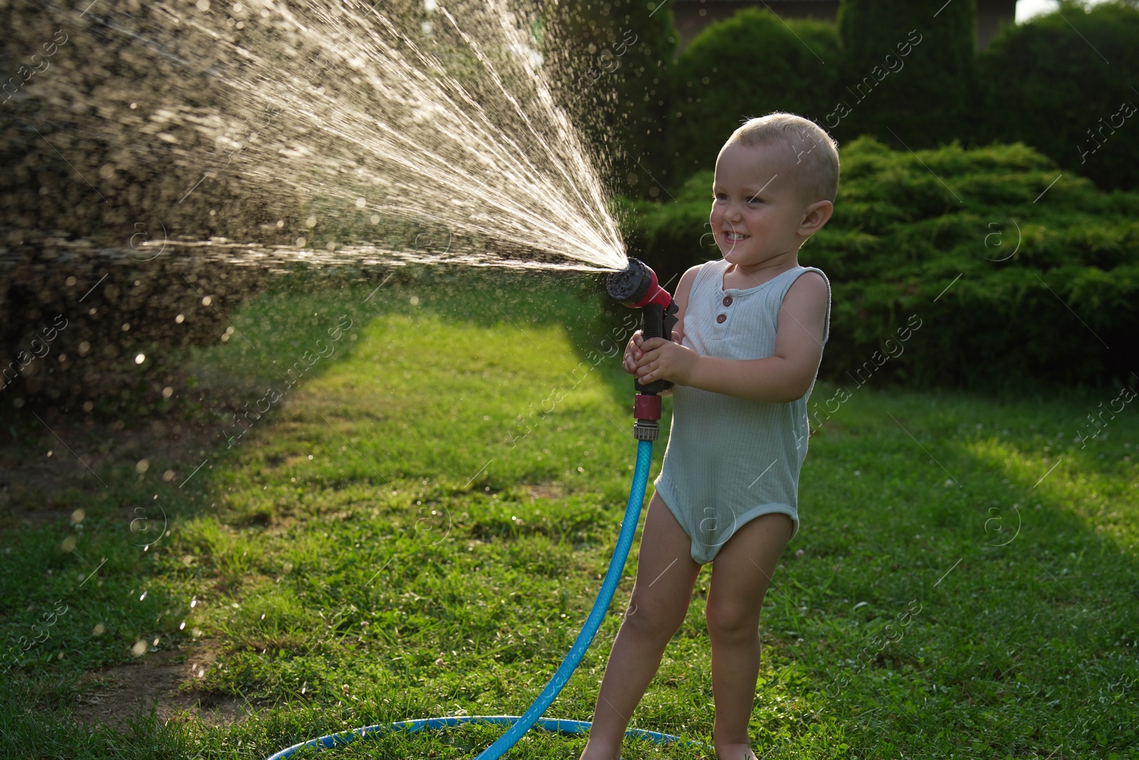 Photo of Little boy watering lawn with hose in backyard